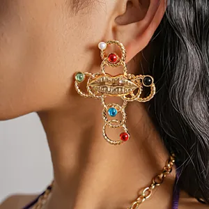 Close-up of vintage gold cross earrings with lip motif and colorful resin stones on model.