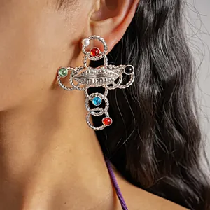 Close-up detail of a silver retro cross earring with lip design and colorful stones.
