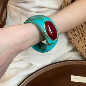 Close-up detail of bohemian teal acrylic bangle featuring a large red oval stone inlay