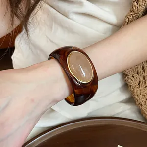 Detailed view of an amber acrylic bangle with an oval beige stone inlay on a model's wrist
