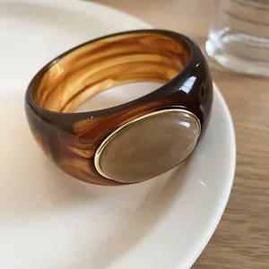 Macro detail of amber acrylic bangle with beige oval stone inlay on a white plate