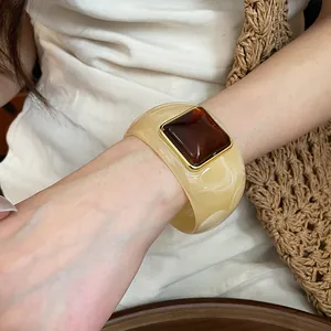 Macro view of a stylish cream acrylic bangle with a square amber resin centerpiece.