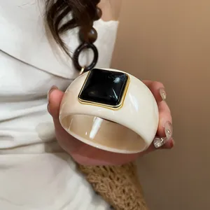 Close-up of a wide ivory acrylic bangle featuring a gold-framed black square centerpiece