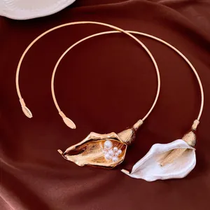 Primo piano di eleganti girocollo a forma di calla dorati e bianchi con perle su raso marrone