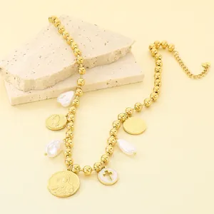 Vue détaillée des breloques religieuses et perles baroques sur un collier doré chic.