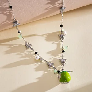Close-up detail of star pearl necklace featuring a green enamel apple pendant with smiley face