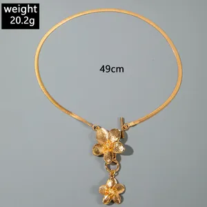 Detail view of a gold-colored flower pendant on a flat snake chain anklet/necklace.