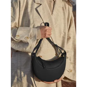 Elegant black leather crescent saddle bag with gold zipper shown on a beige blazer