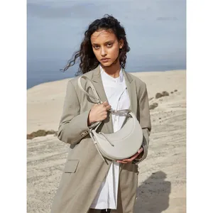 Minimalist beige leather half-moon crossbody bag shown in outdoor desert setting
