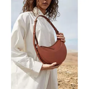 Brown leather crescent crossbody bag with white stitching detail and adjustable strap