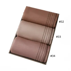 Close-up of three earth-toned jersey scarves with diamond accents in a display box