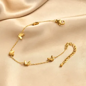 Détail des breloques papillon dorées et de la chaîne sur du tissu satin champagne