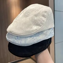 Close-up detail of three stylish textured flat caps in off-white, light blue, and black colors