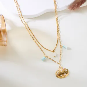 Detalle del collar de doble capa dorado con colgante de concha y dijes de estrella.