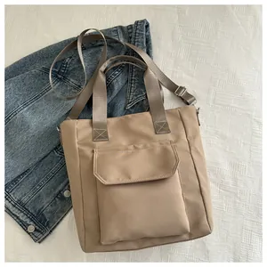 Detailed view of a khaki nylon tote bag featuring a front flap pocket on white fabric.