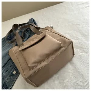 Detail view of a khaki nylon tote bag showing the front flap pocket and fabric texture