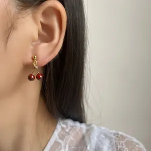 Red pomegranate cherry drop earrings worn by a model in a soft natural light setting