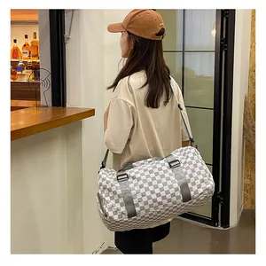 Model carrying a large grey and white checkerboard travel duffel bag in a cafe
