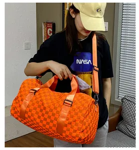 Large orange checkered travel duffel bag held by a model for size reference