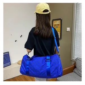 Large capacity blue checkered travel duffel bag shown on shoulder of a model indoors