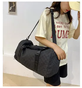 Model carrying a large black quilted travel duffle bag with a shoulder strap and handles