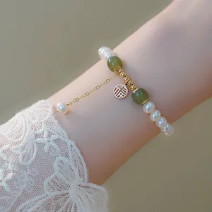 Gros plan d'un bracelet en perles et jade avec breloque dorée "Fu" porté au poignet.