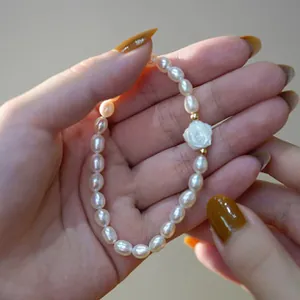Gros plan d'un bracelet en perles d'eau douce avec un charm rose blanche sur la main.