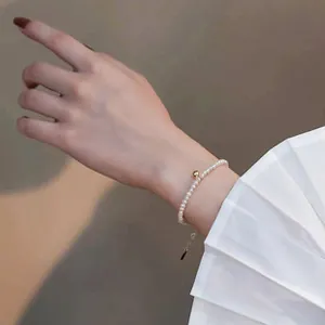 Bracelet élégant en perles d'eau douce avec une bille dorée au poignet féminin.