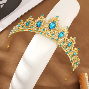 Detailed view of golden crystal bridal tiara with blue water drop rhinestones on a stand