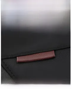 Detail of contrast color leather label on black nylon backpack with neat stitching