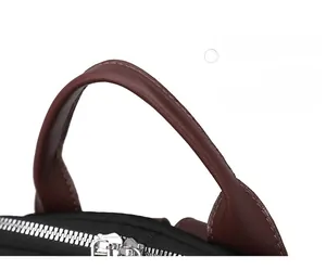Detail of contrast brown PU handle and dual silver metal zippers on black nylon backpack