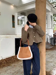 Brown faux suede tote bag with white plush trim detail held by model in city street