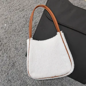 White faux shearling tote bag with brown leather straps on a textured grey background