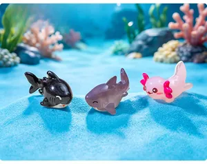 Detailed close-up view of miniature ceramic axolotl and shark figurines on blue sand.