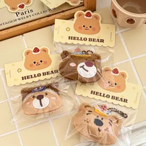 Drie schattige pluche beer sleutelhangers met geborduurde hoeden op beige tegels