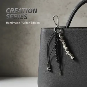 Detailed macro shot of an irregular metal and black bead keychain hanging on a grey bag