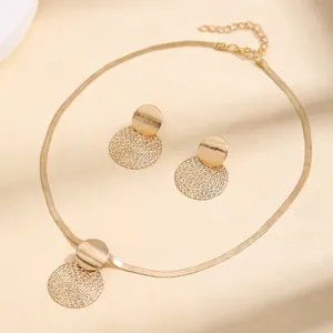 Detailed shot of golden flat snake chain necklace and geometric spiral disc earrings