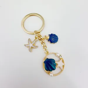 Close-up of a golden ocean-themed keychain featuring blue shell and white starfish charms