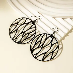 Close-up of black irregular cutout circle dangle earrings with geometric pattern.