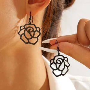 Elegant black cutout rose flower drop earrings shown on model ear and held in hand