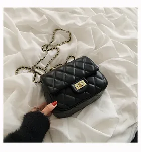 Detail of black quilted chain bag with gold metal lock on white fabric background