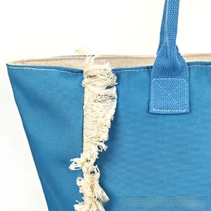 Close-up of blue canvas tote bag featuring cream fringe detail and woven handles
