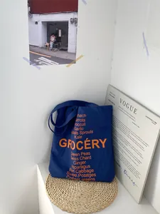 Detailed close-up of dark blue canvas tote bag with orange grocery text and VOGUE magazine