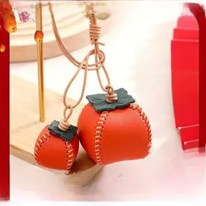 Detail of DIY orange persimmon leather charms with hand-stitched leaf and strap details