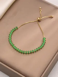 Dettaglio del bracciale dorato regolabile con zirconi verdi su sfondo di seta