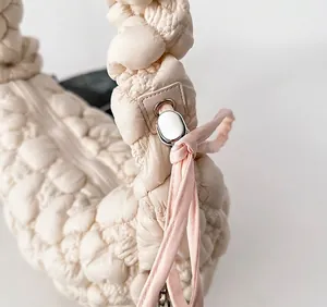 Close-up of cream quilted cloud bag featuring adjustable strap and pink knot detail