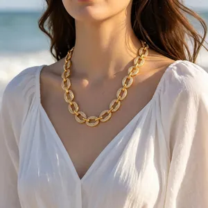 Close-up of a gold-toned pavé link chain necklace worn on a model at the beach
