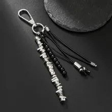 Detail of punk silver metal keychain with black beads and tassel charms on dark background
