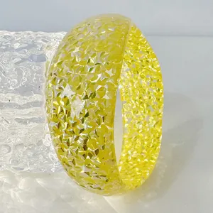 Macro detail of a chunky yellow resin bangle filled with sparkling glitter sequins.
