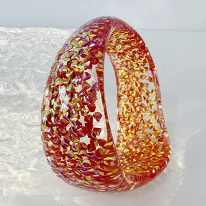 Close-up of a chunky resin bangle filled with colorful glitter and red shards.